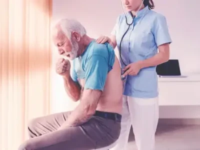 Starszy pan kaszlący w rękę podczas gdy lekarka bada go stetoskopem