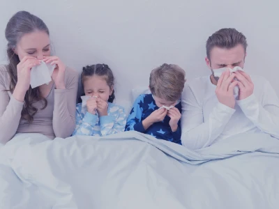 Przeziębiona rodzina siedząca w łóżku i dmuchająca nosy w chusteczki