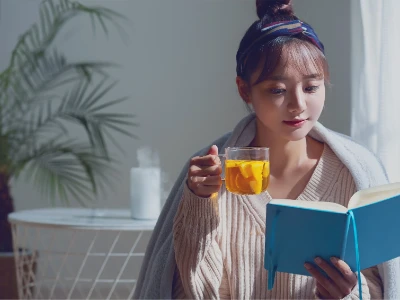 Kobieta okryta kocem czyta książkę i pije herbatę