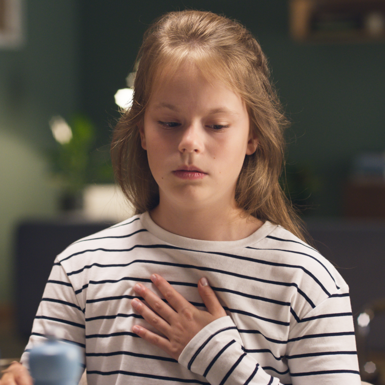 Małe dziecko siedzące przy stole w piżamce i kaszlące w piąstkę, w trakcie gdy mama sprawdza mu temperaturę