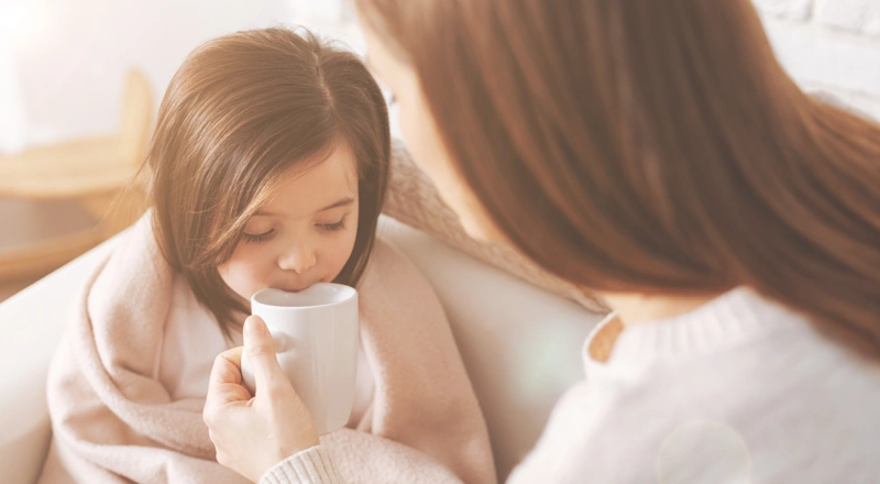 Eine junge Frau mit Pferdeschwanz und geschlossenen Auge im Profil. In der Hand hält sie eine Tasse Tee.